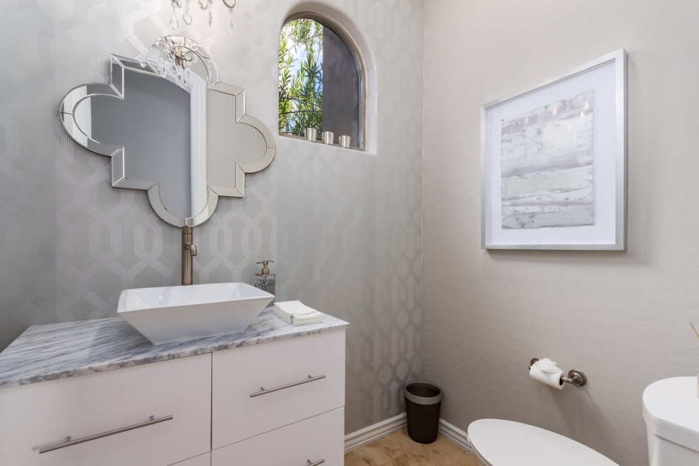 Idées déco pour un petit WC et toilettes classique avec un placard à porte plane, des portes de placard blanches, un mur gris, un sol en travertin, une vasque, un plan de toilette en marbre, un sol beige et un plan de toilette blanc.