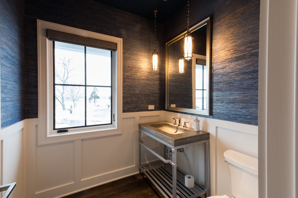 Lantlig inredning av ett litet toalett, med en toalettstol med separat cisternkåpa, ett piedestal handfat, öppna hyllor, grå skåp, blå väggar, mörkt trägolv, bänkskiva i betong och brunt golv