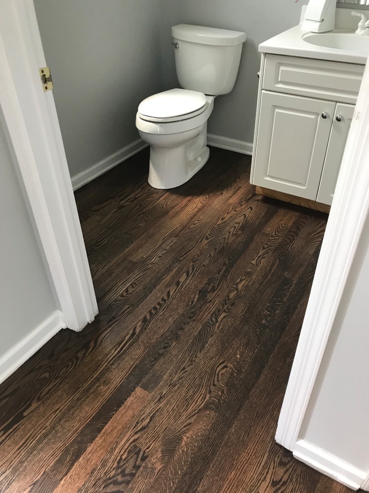 Exempel på ett litet amerikanskt toalett, med luckor med upphöjd panel, vita skåp, en toalettstol med separat cisternkåpa, grå väggar, mellanmörkt trägolv, ett undermonterad handfat, bänkskiva i kvarts och brunt golv