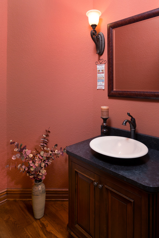 Пример оригинального дизайна: маленький туалет в классическом стиле с фасадами островного типа, темными деревянными фасадами, оранжевыми стенами, паркетным полом среднего тона, настольной раковиной, столешницей из гранита, коричневым полом и черной столешницей для на участке и в саду