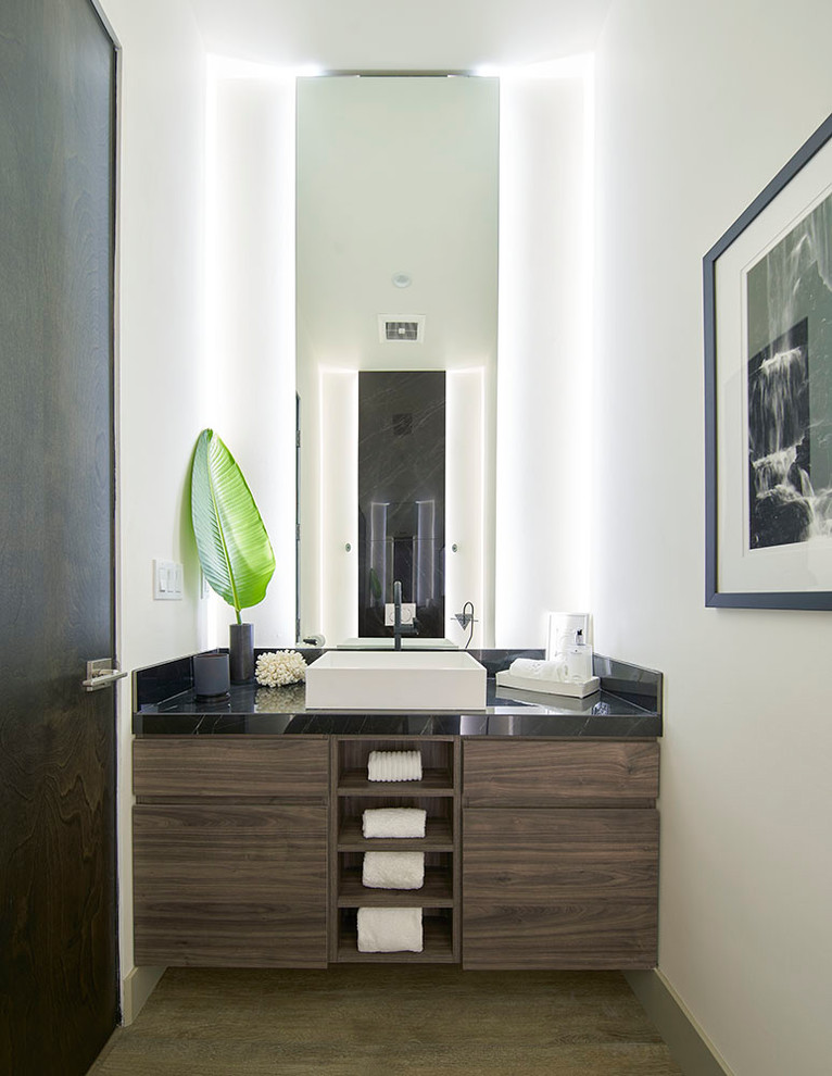 ロサンゼルスにあるコンテンポラリースタイルのおしゃれなトイレ・洗面所 (フラットパネル扉のキャビネット、濃色木目調キャビネット、白い壁、ベッセル式洗面器、黒い洗面カウンター) の写真