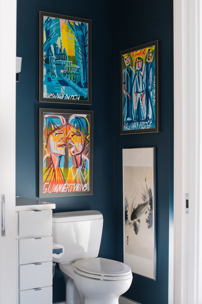 Modern inredning av ett mellanstort vit vitt toalett, med släta luckor, vita skåp, en toalettstol med separat cisternkåpa, blå väggar och bänkskiva i kvarts