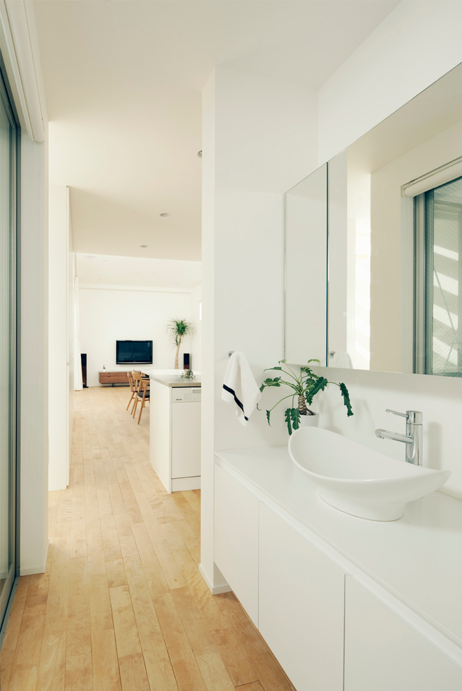 Inredning av ett modernt toalett, med släta luckor, vita skåp, vita väggar, ett fristående handfat, ljust trägolv och beiget golv