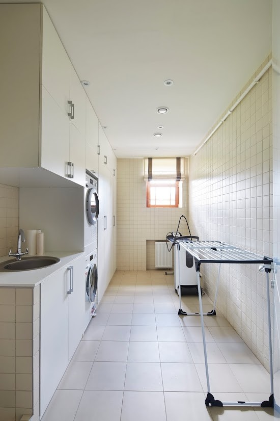 Ejemplo de cuarto de lavado lineal contemporáneo con fregadero encastrado, armarios con paneles lisos, puertas de armario blancas, paredes blancas, lavadora y secadora apiladas y suelo blanco
