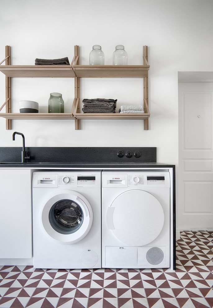 Exempel på en stor minimalistisk linjär tvättstuga enbart för tvätt, med en undermonterad diskho, släta luckor, vita skåp, bänkskiva i kvarts, vita väggar, en tvättmaskin och torktumlare bredvid varandra, flerfärgat golv och klinkergolv i keramik