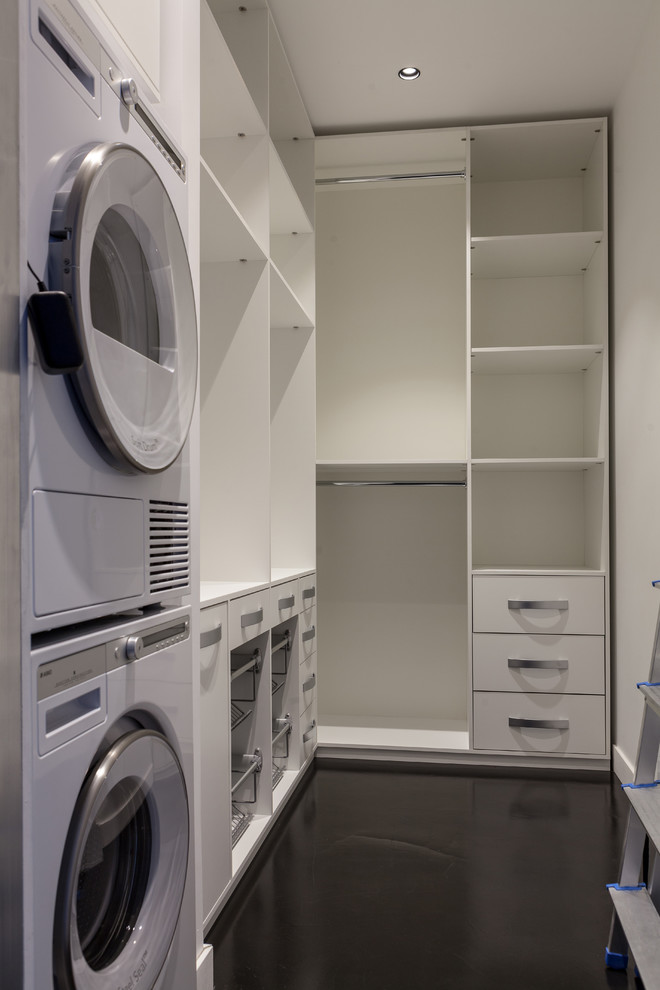 Diseño de armario lavadero en L contemporáneo de tamaño medio con armarios abiertos, puertas de armario blancas, paredes blancas, suelo vinílico, lavadora y secadora apiladas y suelo negro