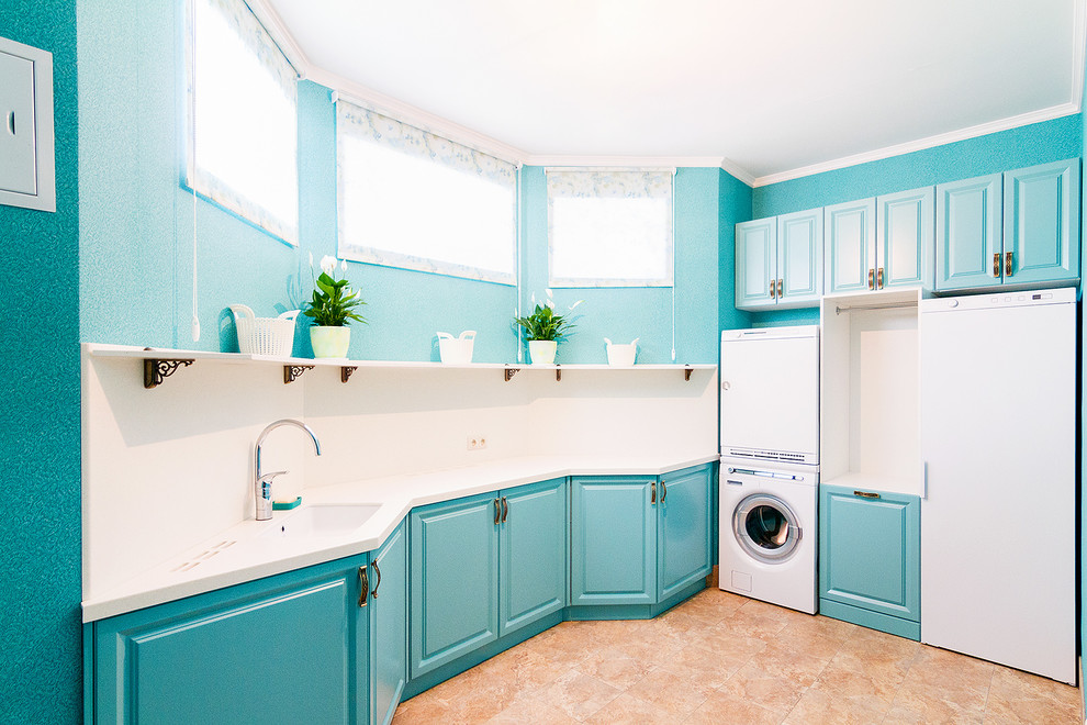 Diseño de cuarto de lavado en L clásico renovado con fregadero bajoencimera, armarios con paneles con relieve, puertas de armario azules, paredes azules, lavadora y secadora apiladas, suelo marrón y encimeras blancas