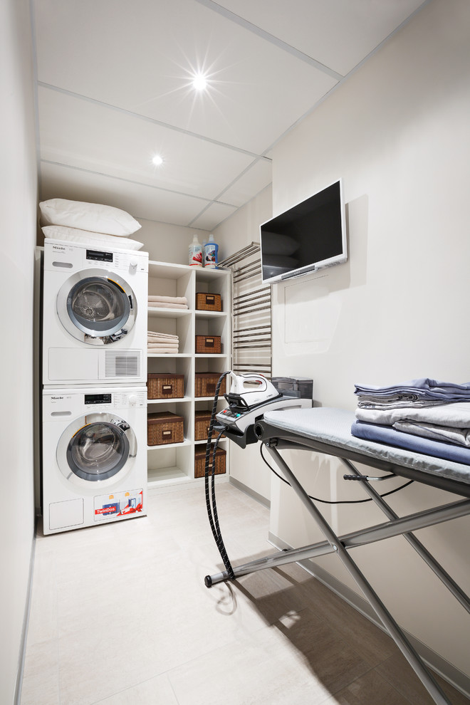 Imagen de cuarto de lavado actual pequeño con paredes blancas, suelo de baldosas de porcelana y lavadora y secadora apiladas