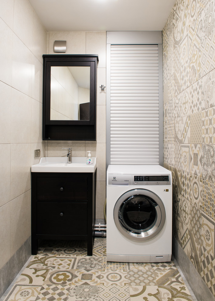 Kleine Moderne Waschküche mit flächenbündigen Schrankfronten, beiger Wandfarbe, Porzellan-Bodenfliesen, schwarzen Schränken, Waschmaschine und Trockner integriert und Waschbecken in Moskau