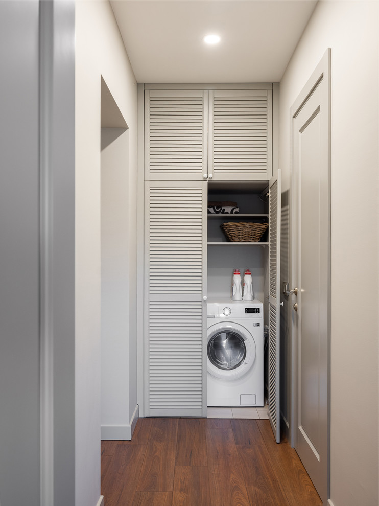 Cette photo montre une buanderie tendance avec un placard, un placard à porte persienne, des portes de placard grises, parquet foncé, un lave-linge séchant et un sol marron.