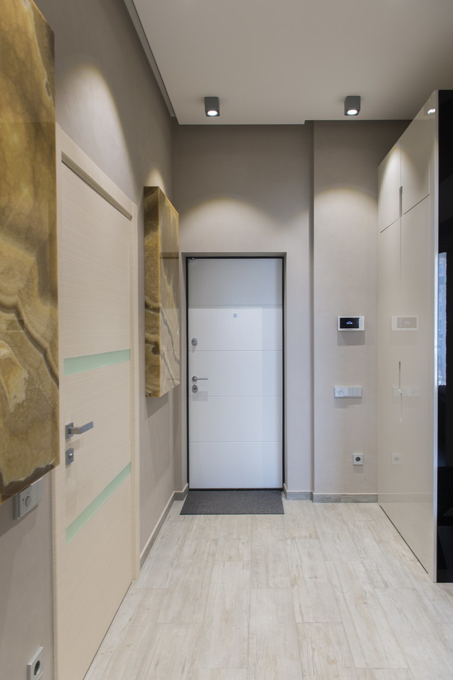 На фото: узкая прихожая среднего размера в современном стиле с серыми стенами, полом из керамогранита, одностворчатой входной дверью, входной дверью из светлого дерева и серым полом