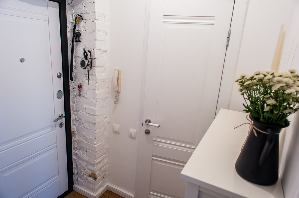 Bild på en liten skandinavisk hall, med vita väggar, laminatgolv, en enkeldörr, en vit dörr och brunt golv