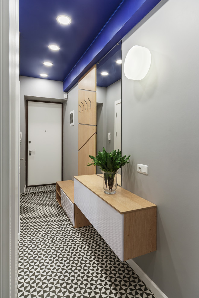 Réalisation d'une petite entrée design avec un couloir, un mur gris, une porte simple, une porte blanche et un sol multicolore.