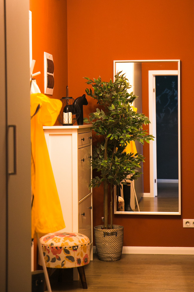 Modelo de puerta principal escandinava pequeña con parades naranjas, suelo laminado, puerta simple, puerta blanca y suelo marrón