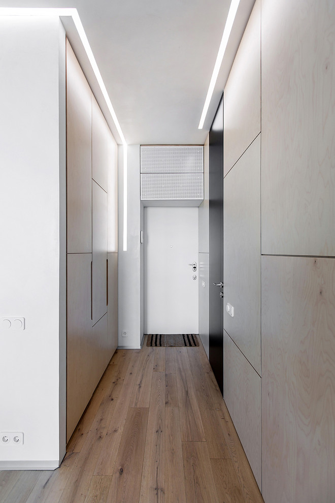 Cette photo montre une entrée tendance avec un mur beige, un sol en bois brun, une porte simple, une porte blanche et un couloir.