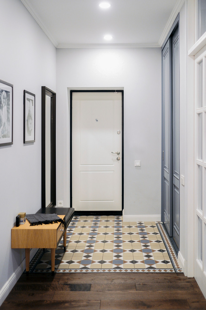 На фото: узкая прихожая в стиле неоклассика (современная классика) с белыми стенами, одностворчатой входной дверью, белой входной дверью, бетонным полом и разноцветным полом с