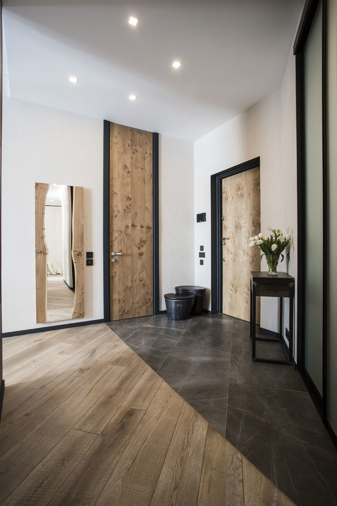 Imagen de entrada contemporánea con paredes blancas, puerta simple, puerta de madera clara y suelo marrón