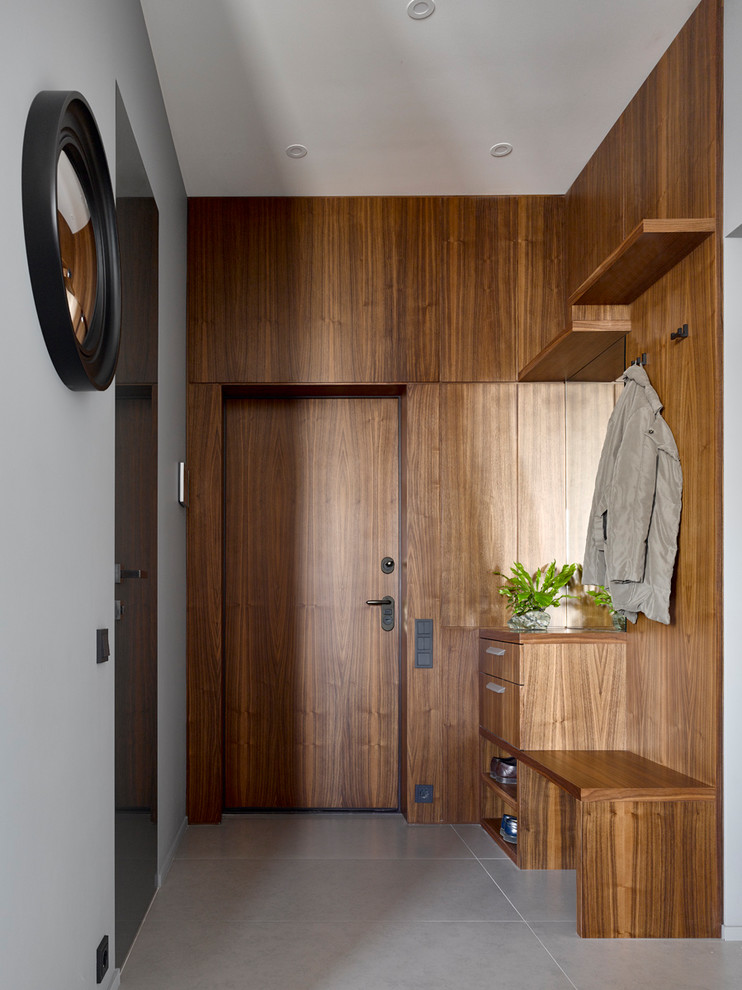 Идея дизайна: входная дверь в стиле модернизм с коричневыми стенами, одностворчатой входной дверью, входной дверью из дерева среднего тона, серым полом и панелями на стенах