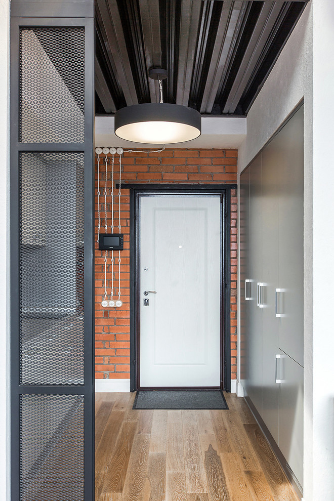 Industriell inredning av en ingång och ytterdörr, med bruna väggar, mellanmörkt trägolv, en enkeldörr och en vit dörr