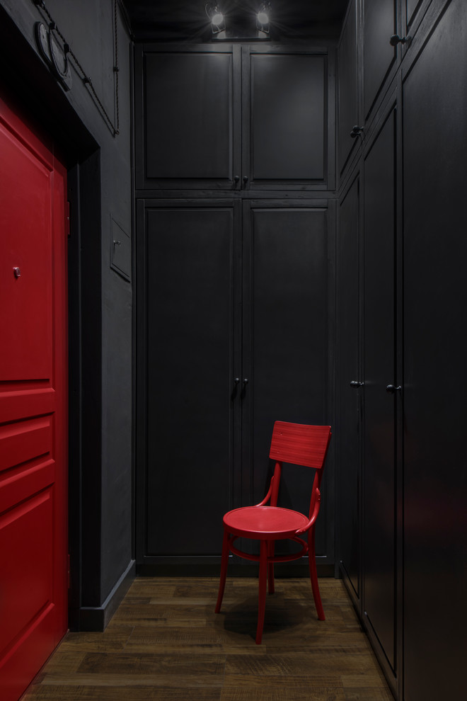 Bild på en mellanstor industriell hall, med svarta väggar, laminatgolv, en enkeldörr, en röd dörr och brunt golv