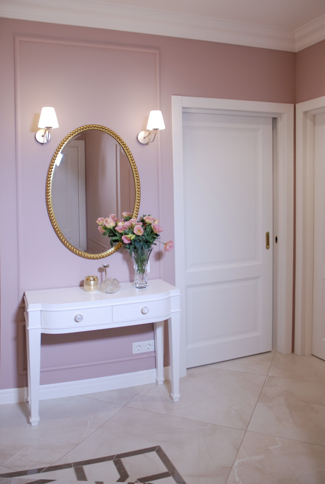 На фото: большая прихожая в стиле неоклассика (современная классика) с розовыми стенами, полом из керамогранита, одностворчатой входной дверью, белой входной дверью и бежевым полом с