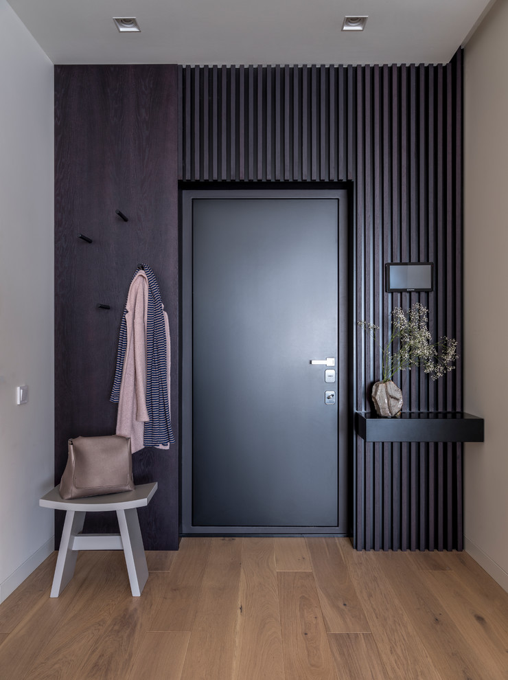 Aménagement d'une porte d'entrée contemporaine avec un mur noir, un sol en bois brun, une porte simple, une porte noire et un sol marron.