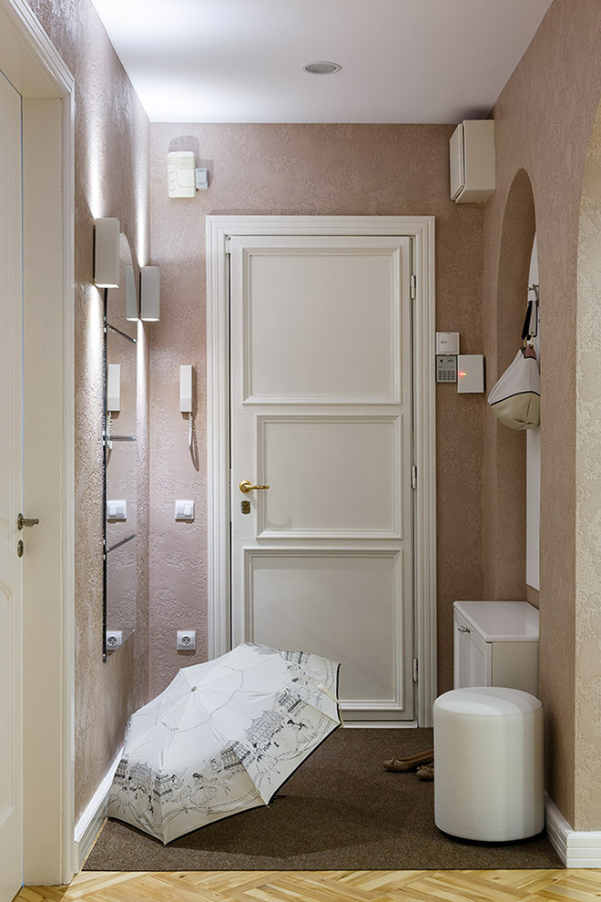 Inredning av en klassisk liten ingång och ytterdörr, med rosa väggar, ljust trägolv, en enkeldörr, en vit dörr och beiget golv