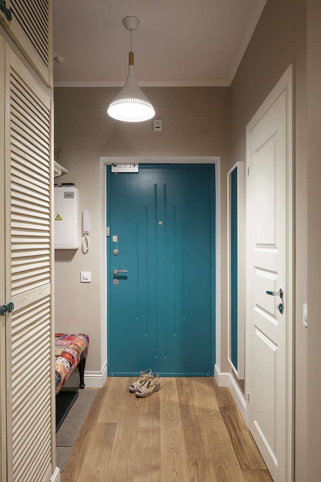 Cette image montre une petite porte d'entrée design avec un mur gris, un sol en bois brun, une porte simple, une porte bleue et un sol marron.