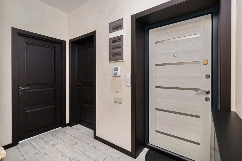 Modelo de hall pequeño con paredes beige, suelo laminado, puerta simple, puerta de madera clara y suelo beige