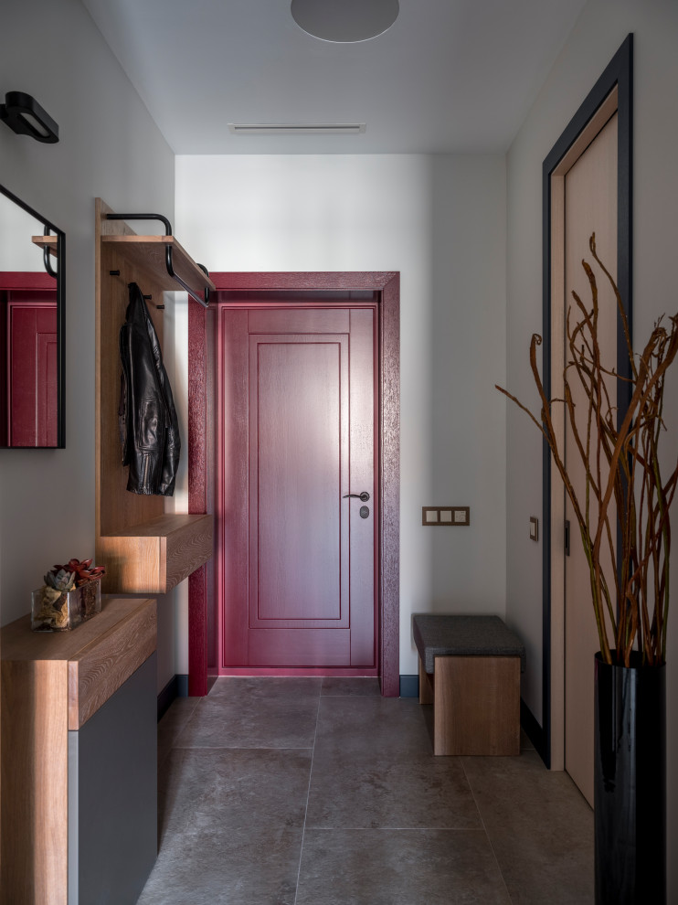 Cette image montre une porte d'entrée design avec un mur blanc, une porte simple, une porte rouge et un sol gris.