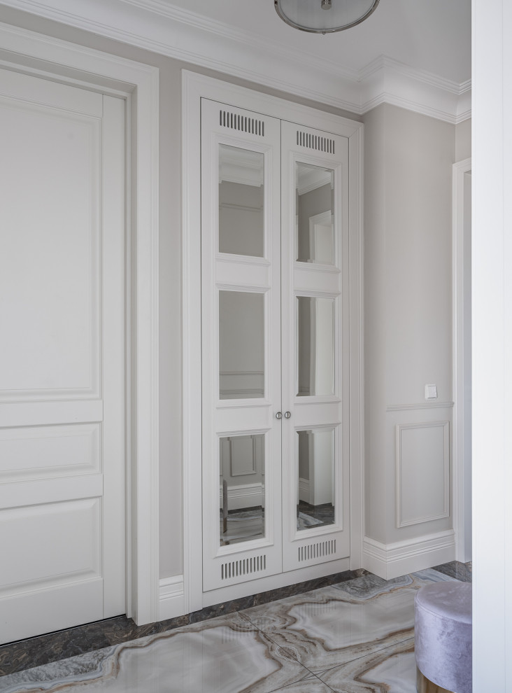 Стильный дизайн: узкая прихожая среднего размера в стиле неоклассика (современная классика) с серыми стенами, полом из керамогранита, одностворчатой входной дверью, входной дверью из дерева среднего тона и синим полом - последний тренд