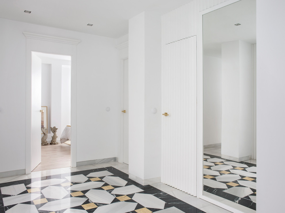 На фото: большой коридор в средиземноморском стиле с белыми стенами, мраморным полом, белым полом и панелями на стенах с