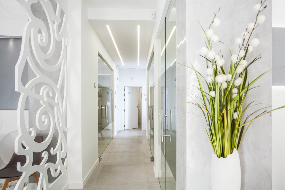 Cette photo montre un grand couloir moderne avec un mur blanc, un sol en carrelage de céramique et un sol gris.