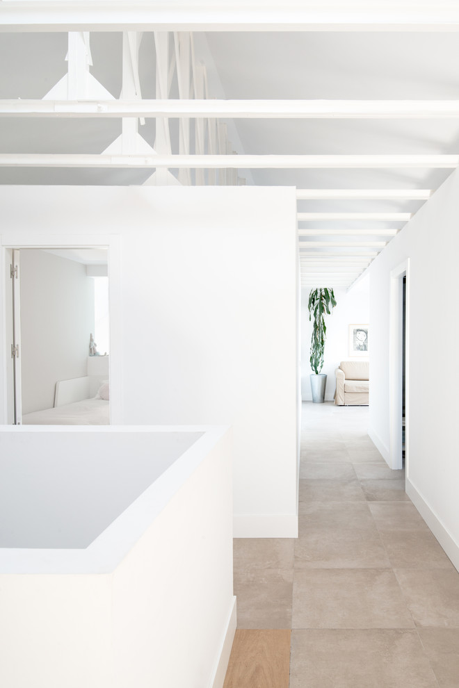 На фото: большой коридор в средиземноморском стиле с белыми стенами, полом из керамической плитки и серым полом с