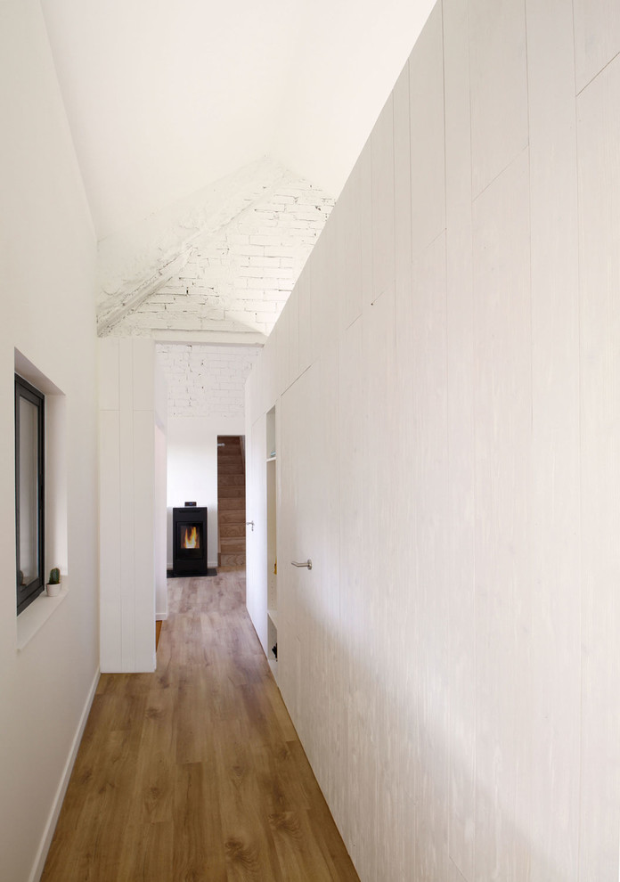 Пример оригинального дизайна: маленький коридор в скандинавском стиле с белыми стенами, полом из ламината и коричневым полом для на участке и в саду