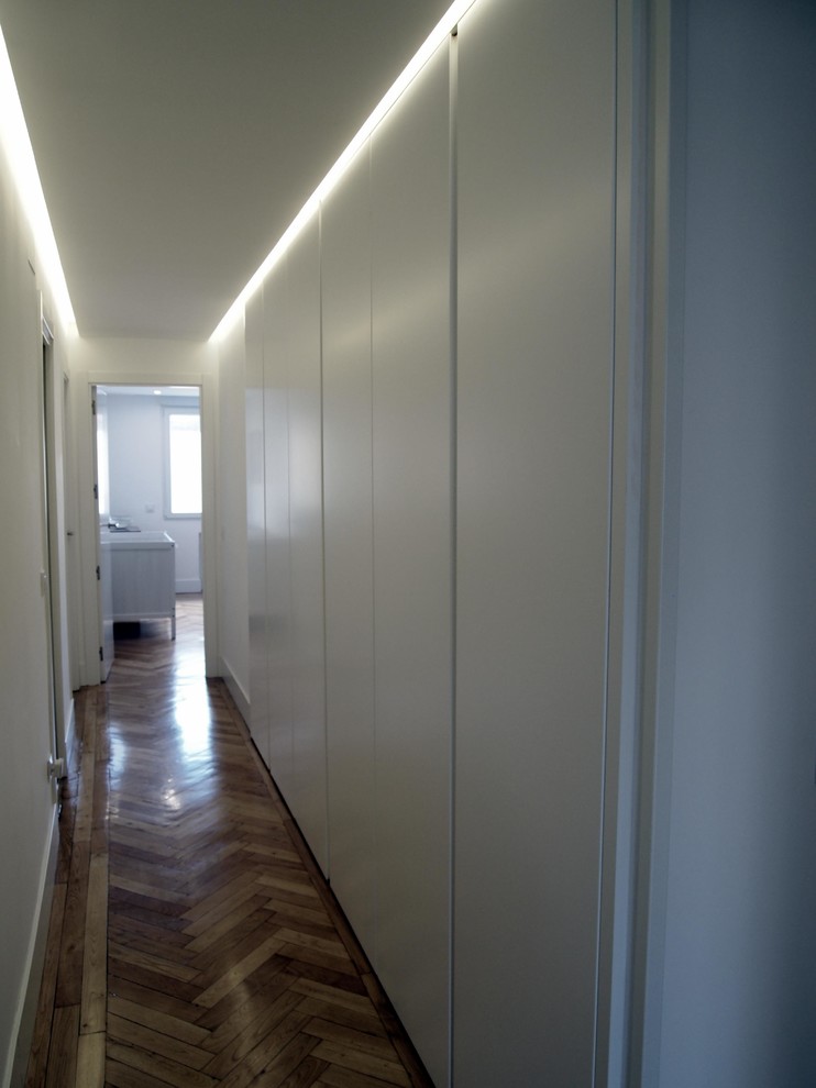 Cette photo montre un couloir tendance avec un mur blanc, un sol en bois brun et un sol marron.