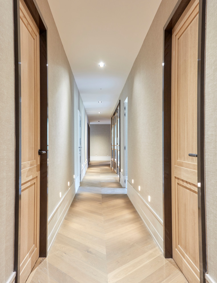 На фото: большой коридор в стиле неоклассика (современная классика) с бежевыми стенами, светлым паркетным полом, коричневым полом и обоями на стенах с