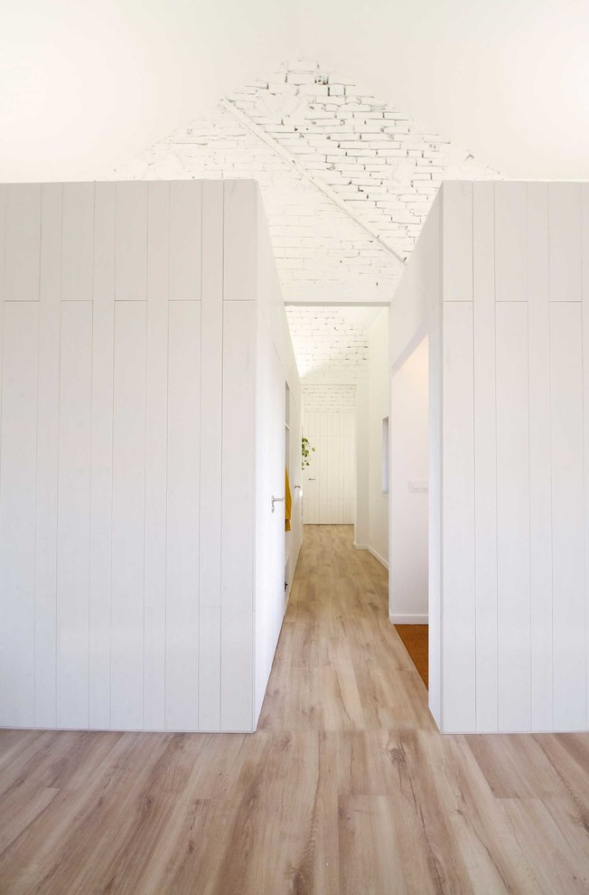 Minimalistisk inredning av en hall, med vita väggar, ljust trägolv och brunt golv