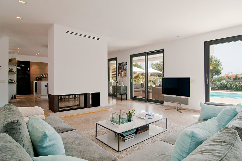 Example of a large tuscan open concept limestone floor family room design in Palma de Mallorca with white walls, a tv stand and a two-sided fireplace