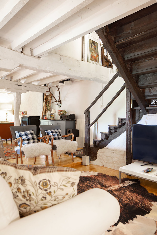 Ejemplo de sala de estar con rincón musical abierta rural de tamaño medio con paredes blancas, suelo de madera clara, suelo marrón y televisor retractable