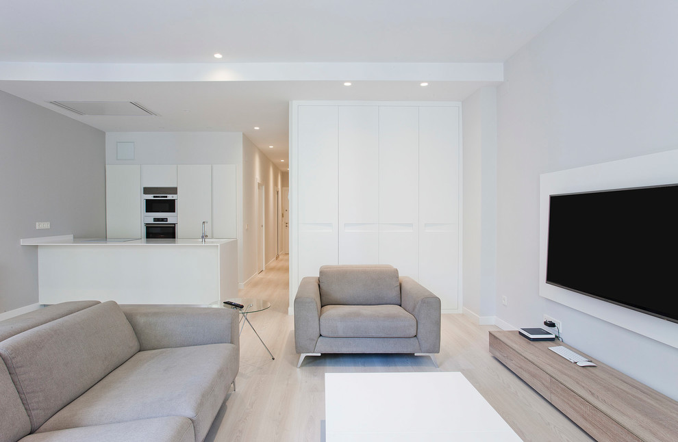 Diseño de sala de estar abierta actual de tamaño medio con paredes blancas, suelo de madera clara, televisor colgado en la pared y suelo beige