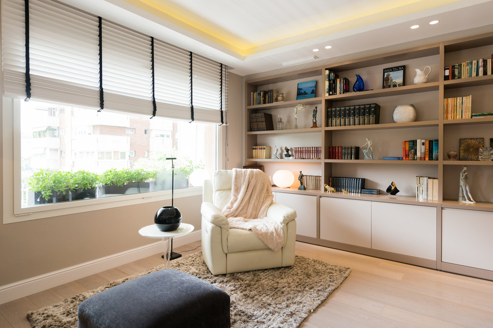 Diseño de sala de estar con biblioteca cerrada moderna de tamaño medio sin chimenea y televisor con paredes beige y suelo de madera clara