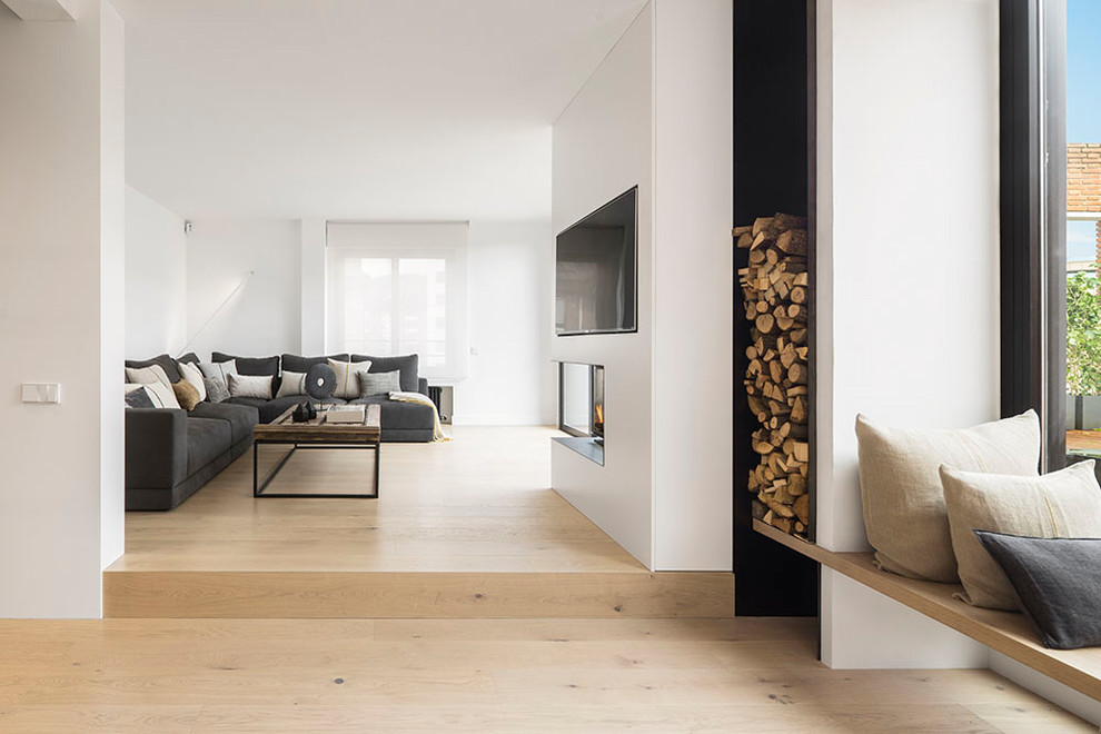 Ejemplo de sala de estar abierta contemporánea grande con paredes blancas, suelo de madera en tonos medios, chimenea de esquina, marco de chimenea de hormigón y televisor colgado en la pared