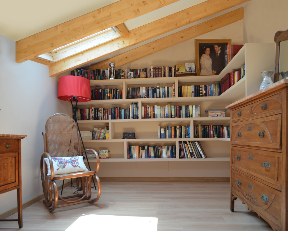 Lantlig inredning av ett litet avskilt allrum, med ett bibliotek, beige väggar och ljust trägolv
