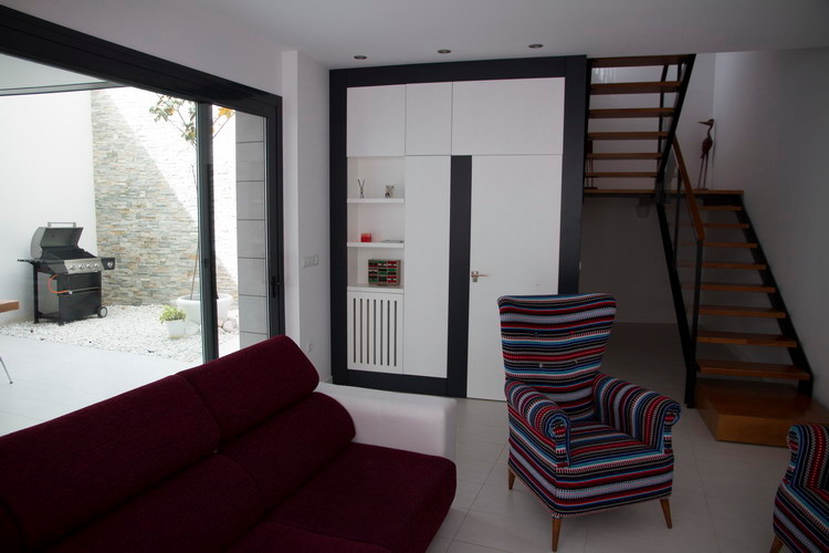 Imagen de sala de estar abierta minimalista de tamaño medio sin chimenea con paredes blancas, suelo de baldosas de cerámica y televisor colgado en la pared