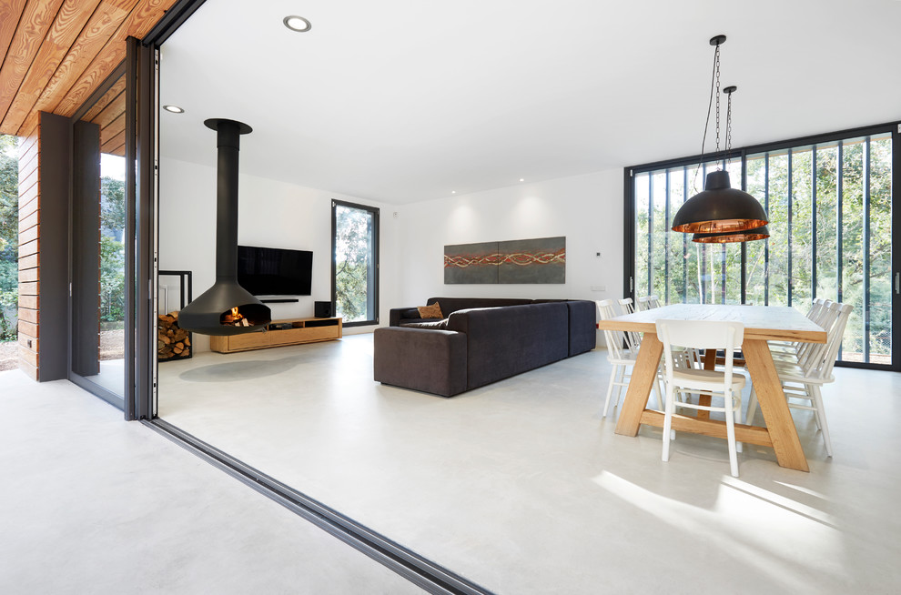 Immagine di un soggiorno design aperto con pareti bianche, pavimento in cemento, camino sospeso, TV a parete e pavimento grigio