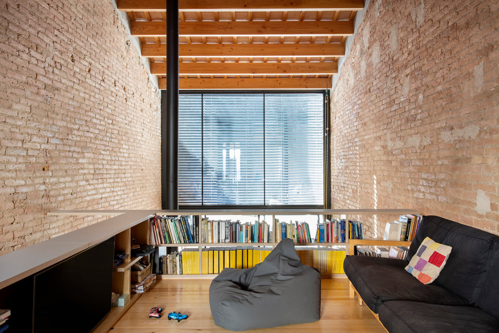 Kleiner Industrial Hobbyraum im Loft-Stil mit roter Wandfarbe, hellem Holzboden, freistehendem TV, beigem Boden, gewölbter Decke und Ziegelwänden in Barcelona