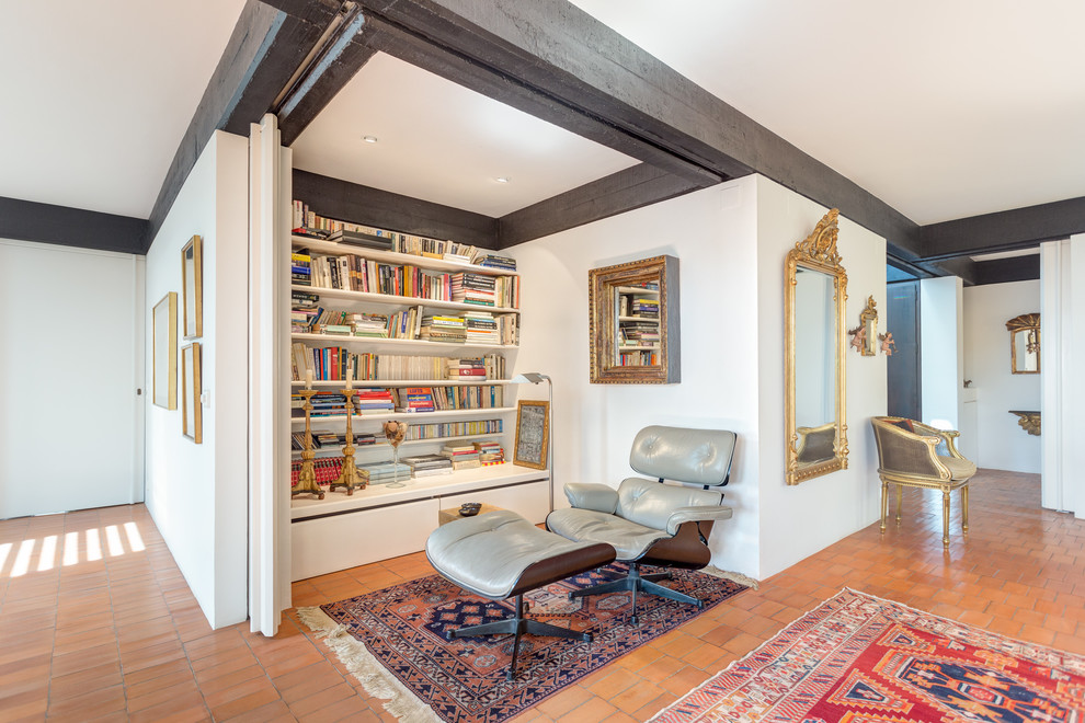 Imagen de sala de estar con biblioteca abierta mediterránea pequeña sin chimenea y televisor con paredes blancas y suelo de baldosas de terracota