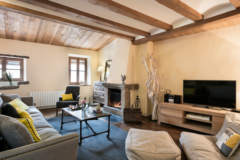 Ejemplo de sala de estar abierta de estilo de casa de campo de tamaño medio con paredes amarillas, suelo de madera oscura, todas las chimeneas, marco de chimenea de piedra y pared multimedia