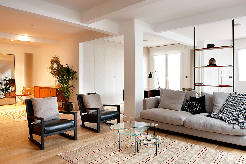 Modelo de sala de estar abierta actual grande sin chimenea y televisor con paredes blancas y suelo de madera clara